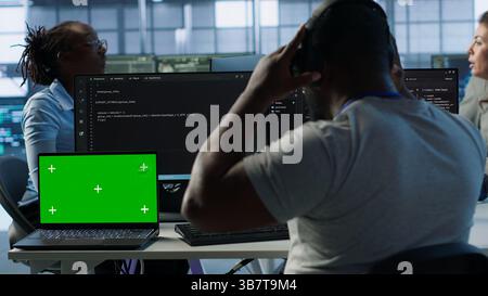 Isolated screen laptop next to programmer coding in server farm while listening music in headphones. Worker safeguarding hardware against unauthorized access with chroma key notebook, camera A Stock Photo