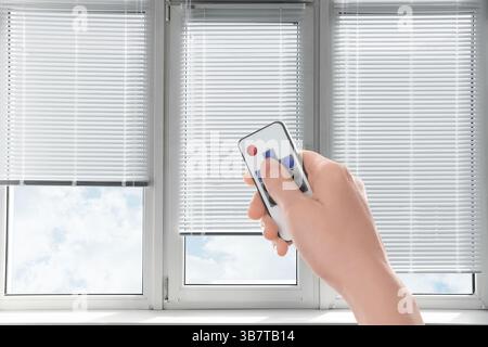 Woman using remote to control blinds in room, closeup Stock Photo