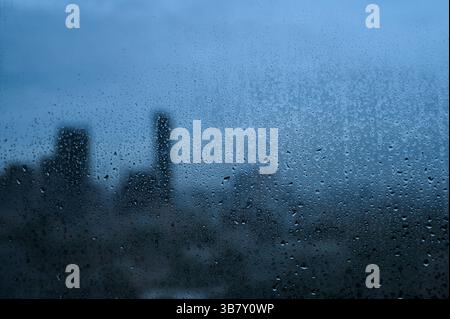 Raindrops on glass with soft city silhouette background. Stock Photo