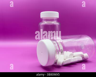 Two transparent jars with white pills, one jar is in the foreground, on a pink background, front view. Stock Photo
