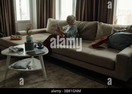 Senior Lady Sitting on Couch Using Smartphone in Living Room Stock Photo