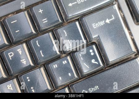 This detailed close up highlights the 'Enter' key and several other keys with symbols on a well-used black computer keyboard, capturing its surface te Stock Photo