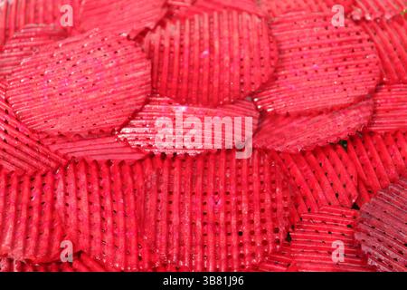 High-angle macro shot showcases a vibrant display of corrugated red potato chips stacked together; their textured surfaces and rich color create a com Stock Photo