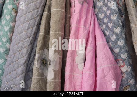 Pastel-colored fabrics are stacked vertically, displaying varied patterns including floral, heart, and geometric quilting. These textiles offer textur Stock Photo