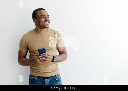 Smiling African American man holding smartphone while looking aside at copy space Stock Photo