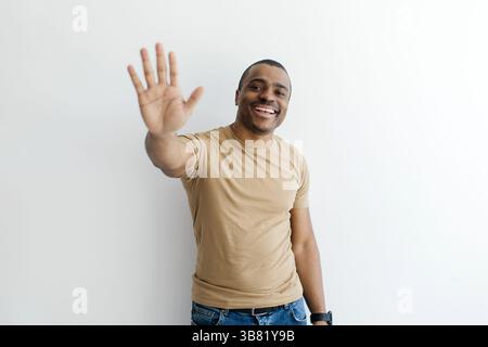 Friendly Black man raising hand in greeting, smiling warmly at the camera Stock Photo