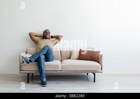 Peaceful African American man sitting comfortably on sofa with hands behind head Stock Photo