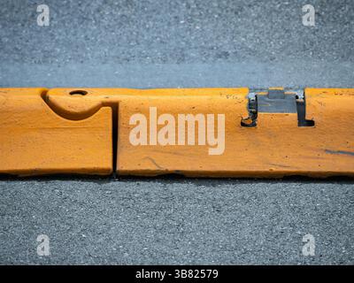 A close-up view of a yellow road barrier on a gray asphalt surface, showcasing its texture and wear. Stock Photo