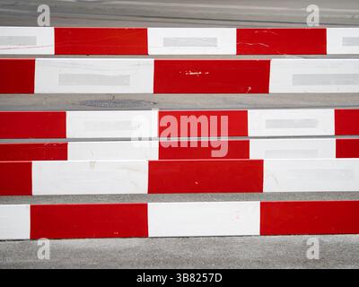 A close-up view of red and white striped barriers on a concrete surface, creating a bold geometric pattern. The image highlights the contrast between Stock Photo