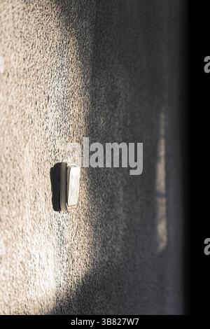 A white wall with a light switch on it. Sunlight illuminates part of the wall Stock Photo