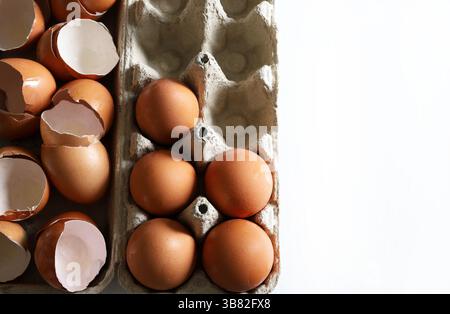 Broken eggshells and whole eggs in a cardboard egg container. Directly above. Copy space. Stock Photo