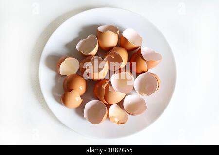 Group of broken eggshells in a white plate isolated on white table. Directly above. Stock Photo