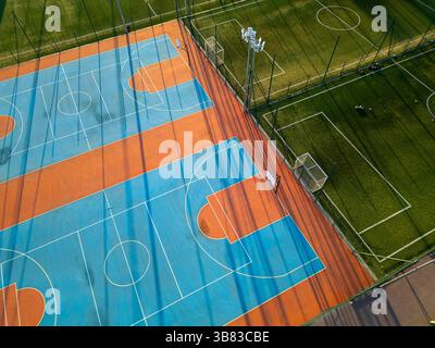 Outdoor basketball and soccer court at sunset with colorful surface, long shadows, and green artificial turf in the background Stock Photo