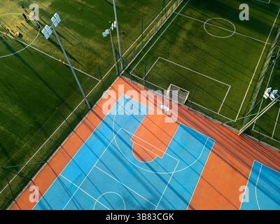 Outdoor basketball and soccer court at sunset with colorful surface, long shadows, and green artificial turf in the background Stock Photo
