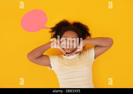 Emotional African-American girl with speech bubble lying on yellow background, top view Stock Photo