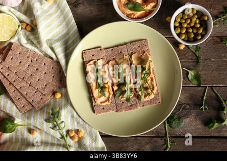 Composition with crispbreads, tasty hummus and green peas on wooden background Stock Photo