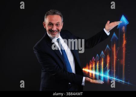 Smiling businessman in suit showcasing an upward digital graph with arrows, symbolizing growth, success and innovation in business. Futuristic style. Stock Photo