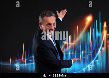 Cheerful businessman in suit showing an exponential growth chart with colorful digital bars and arrows. Concept of success, technology and business ex Stock Photo