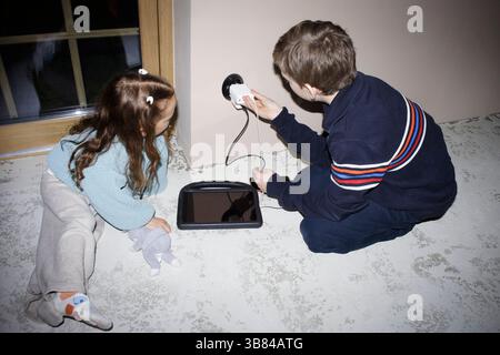 High angle view of siblings charging digital tablet while sitting at home Stock Photo
