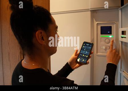 Woman connecting smart phone app with thermostat at home Stock Photo
