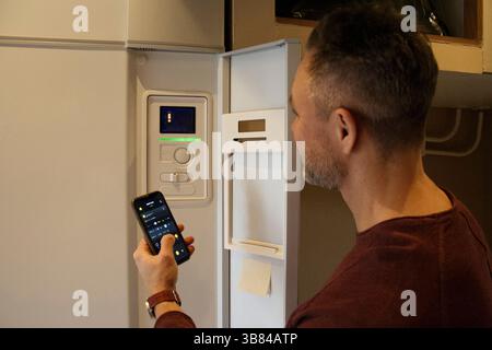 Man connecting smart phone with thermostat through app at home Stock Photo