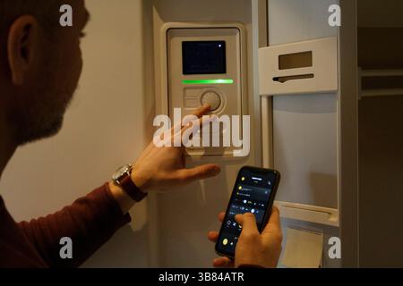 Man adjusting temperature through thermostat while holding smart phone Stock Photo