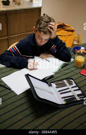 Depressed boy doing homework while sitting at dining table Stock Photo
