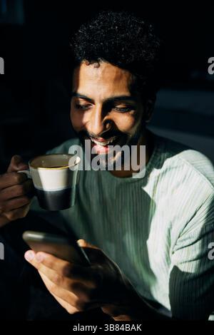Happy man drinking coffee while using smart phone Stock Photo