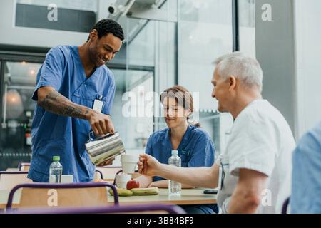 Smiling male nurse pouring coffee for colleague during break in cafeteria at clinic Stock Photo