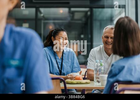 Smiling female doctor talking with colleagues while having breakfast at table in hospital cafeteria Stock Photo