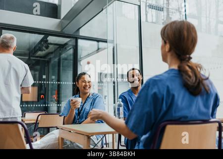 Happy multiracial male and female nurses sitting at table in cafeteria during break Stock Photo