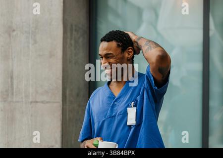 Happy male nurse holding mug with hand behind head standing in clinic Stock Photo