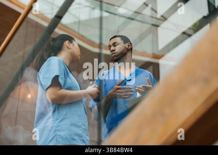 Low angle view of male and female healthcare workers gesturing while discussing with each other at hospital Stock Photo