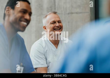 Happy mature male physician enjoying with team in clinic Stock Photo