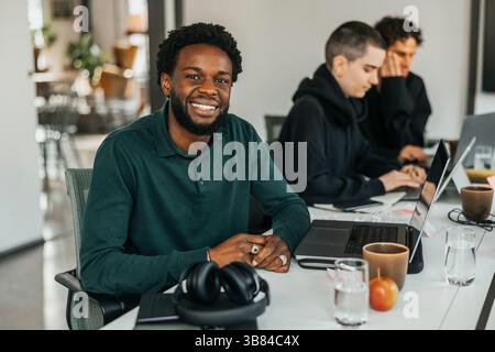Portrait of smiling young businessman sitting with laptop in tech startup office Stock Photo