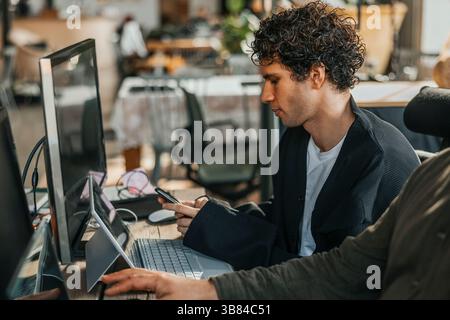 Male computer programmer using smart phone while sitting with wireless technologies in office Stock Photo
