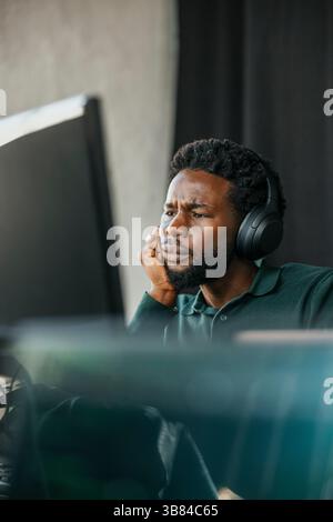Confused male computer programmer wearing wireless headphones working in tech office Stock Photo