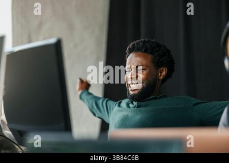 Male computer programmer stretching arms while sitting in tech hub Stock Photo