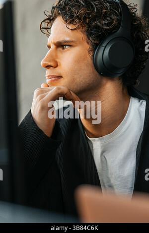Tilted image of focused young computer programmer wearing wireless headphones looking at computer while working in offic Stock Photo