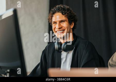 Happy male IT professional with wireless headphones around neck sitting in office Stock Photo