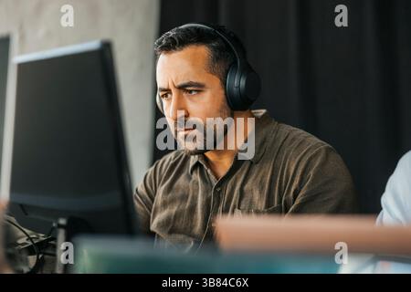 Focused male programmer wearing wireless headphones working on computer in tech startup office Stock Photo