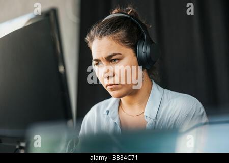 Focused young female programmer wearing wireless headphones using computer in office Stock Photo