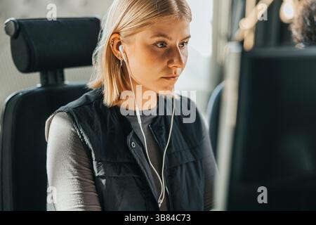Focused young female entrepreneur wearing headphones working on computer in tech office Stock Photo