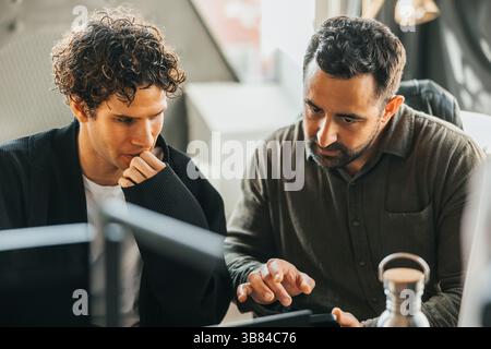 Male computer programmers discussing ideas on smart phone while sitting in office Stock Photo