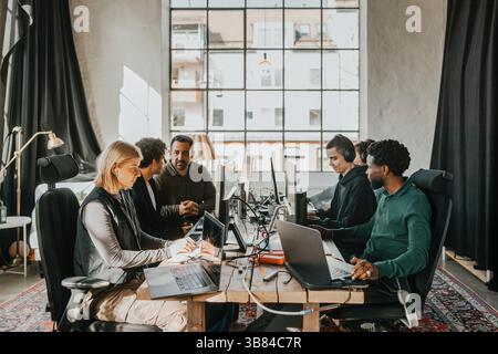 Group of multiracial computer professionals working on desktop PC while sitting at desk in tech startup office Stock Photo