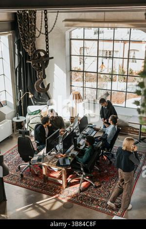 High angle view of IT professionals planning strategies and working on desktop PC in startup office Stock Photo