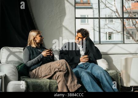 Young male and female computer programmers talking with each other during coffee break while sitting on sofa in office Stock Photo
