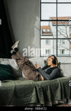 Relaxed young female businesswoman listening to music through wireless headphones while lying on sofa in office Stock Photo