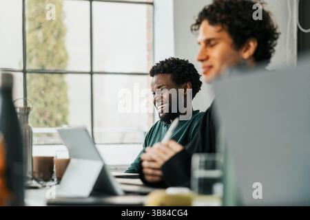 Happy young male software engineer sitting with colleague at desk in tech startup office Stock Photo