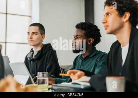 Focused male entrepreneur sitting with coworkers during meeting in tech startup office Stock Photo